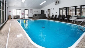 Una piscina interior con agua cristalina, rodeada de sillones de descanso y una escalera que lleva a un nivel superior.