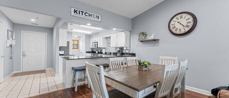 A modern kitchen with white cabinetry, a wooden dining table, and a clock on the wall.