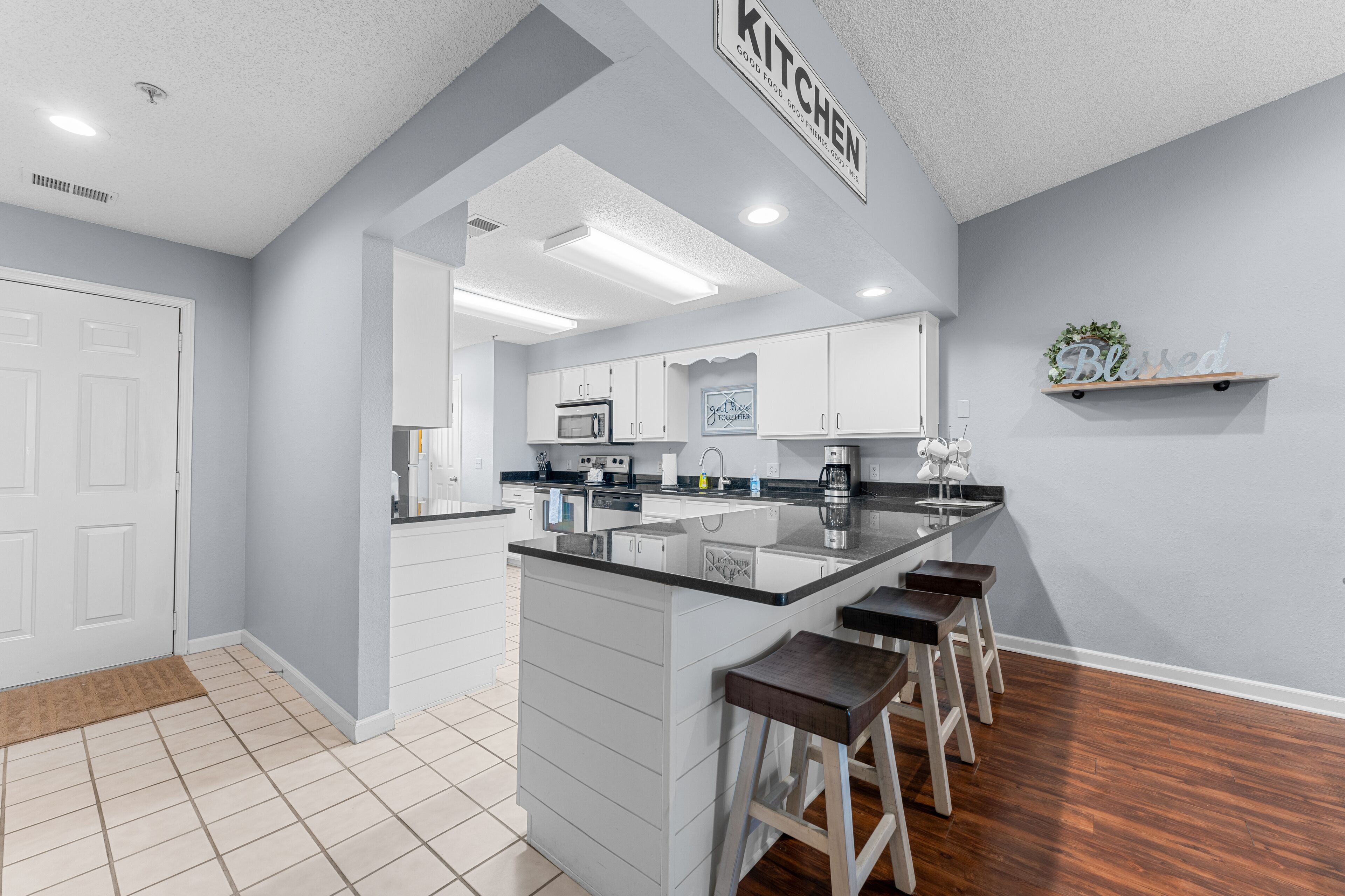 A modern kitchen with white cabinets, a black countertop, and a bar stool area.