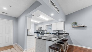 Una cocina moderna con armarios blancos, encimera negra y una zona con taburetes de bar.
