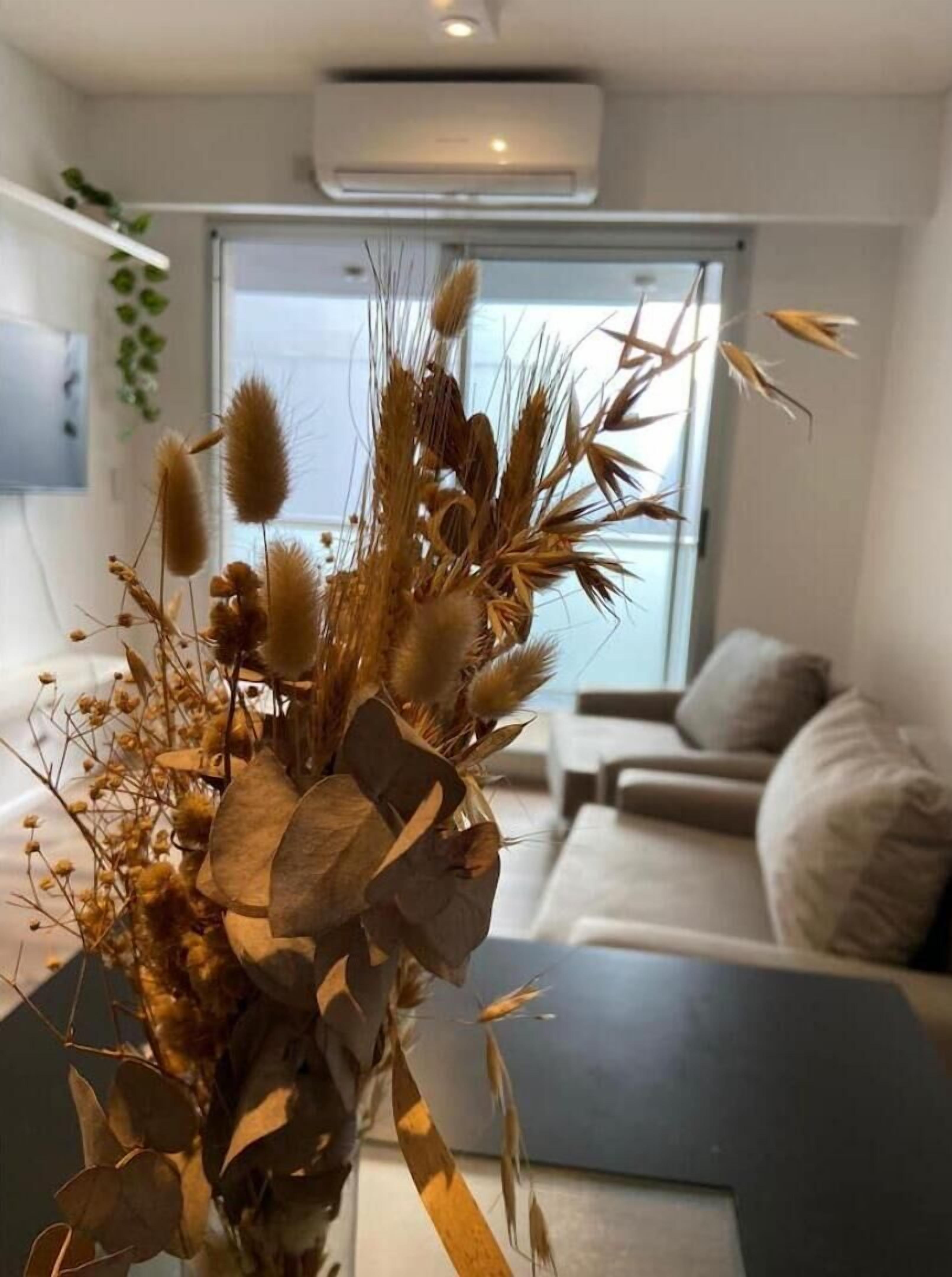 A living room with a modern sofa, a decorative vase with dried plants, and a large window with a view.