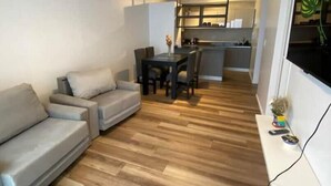 Een moderne woonkamer met een grijze bank, een eettafel met stoelen en een keuken op de achtergrond.