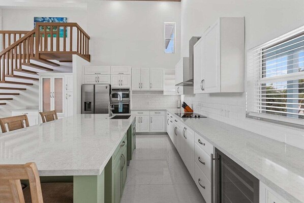 A modern kitchen with white cabinetry, a central island, and a wooden staircase.