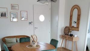 A dining area with a round wooden table, teal chairs, and a woven centerpiece. There is a mirror on the wall and a door with a round window.