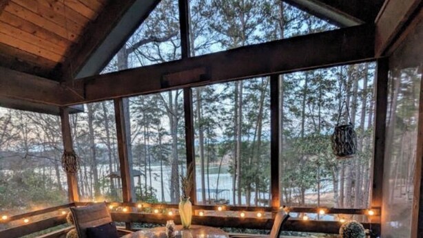 A covered outdoor seating area with a table and chairs, large windows, and string lights. - Cozy 3-bedroom lakefront cottage in beautiful Clemson, SC  (Clemson)