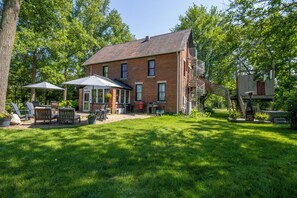 A two-story brick house with a covered patio, a barbecue grill, and a basketball hoop. - Historic Farmhouse with Hot Tub, Treehouse Shower, & Chickens! (Michigan City)