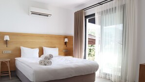 A hotel room with a bed, a nightstand, a lamp, an air conditioning unit, and a window with curtains. - DÖRTMEVSİM PANSİYON (Bodrum)