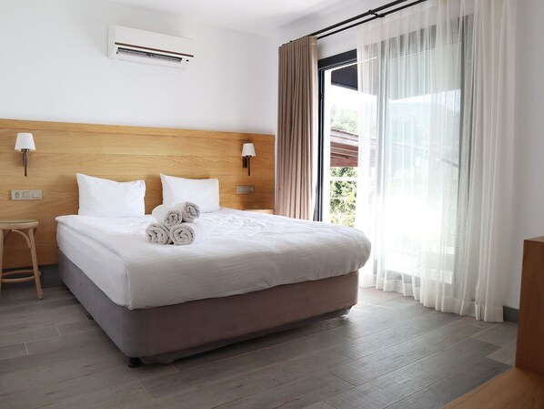 A hotel room with a bed, a nightstand, a lamp, an air conditioning unit, and a window with curtains. - DÖRTMEVSİM PANSİYON (Bodrum)