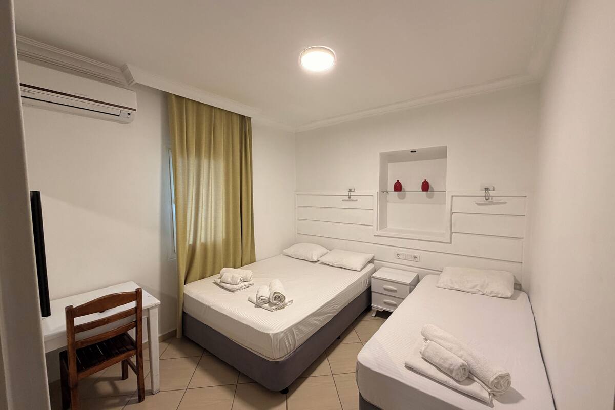 A hotel room with a single bed, a smaller bed, a desk, and a chair.