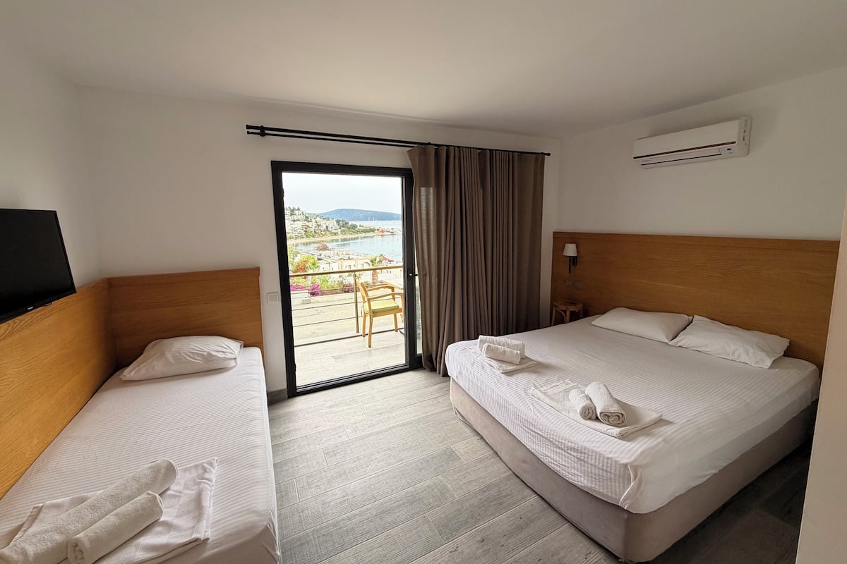 A hotel room with two beds, a TV, an air conditioner, and a balcony with a view.