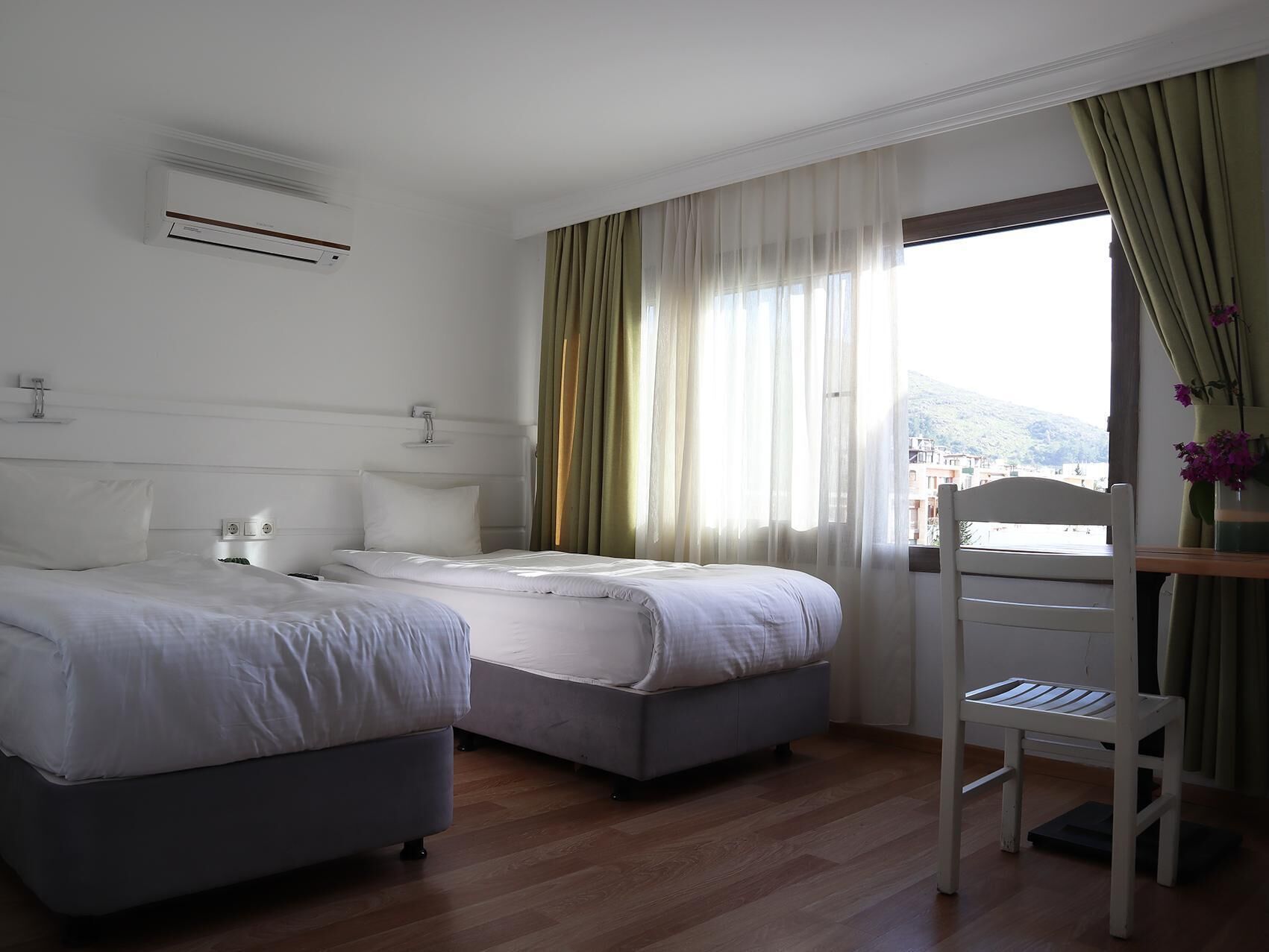 A hotel room with two beds, a desk, and a window with curtains.