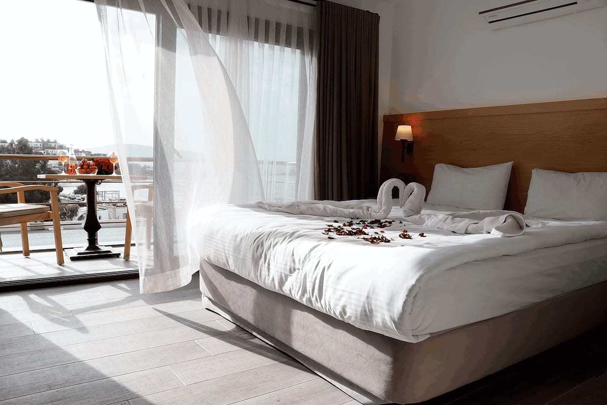 A hotel room with a large bed, a balcony with a table and chairs, and a city view.