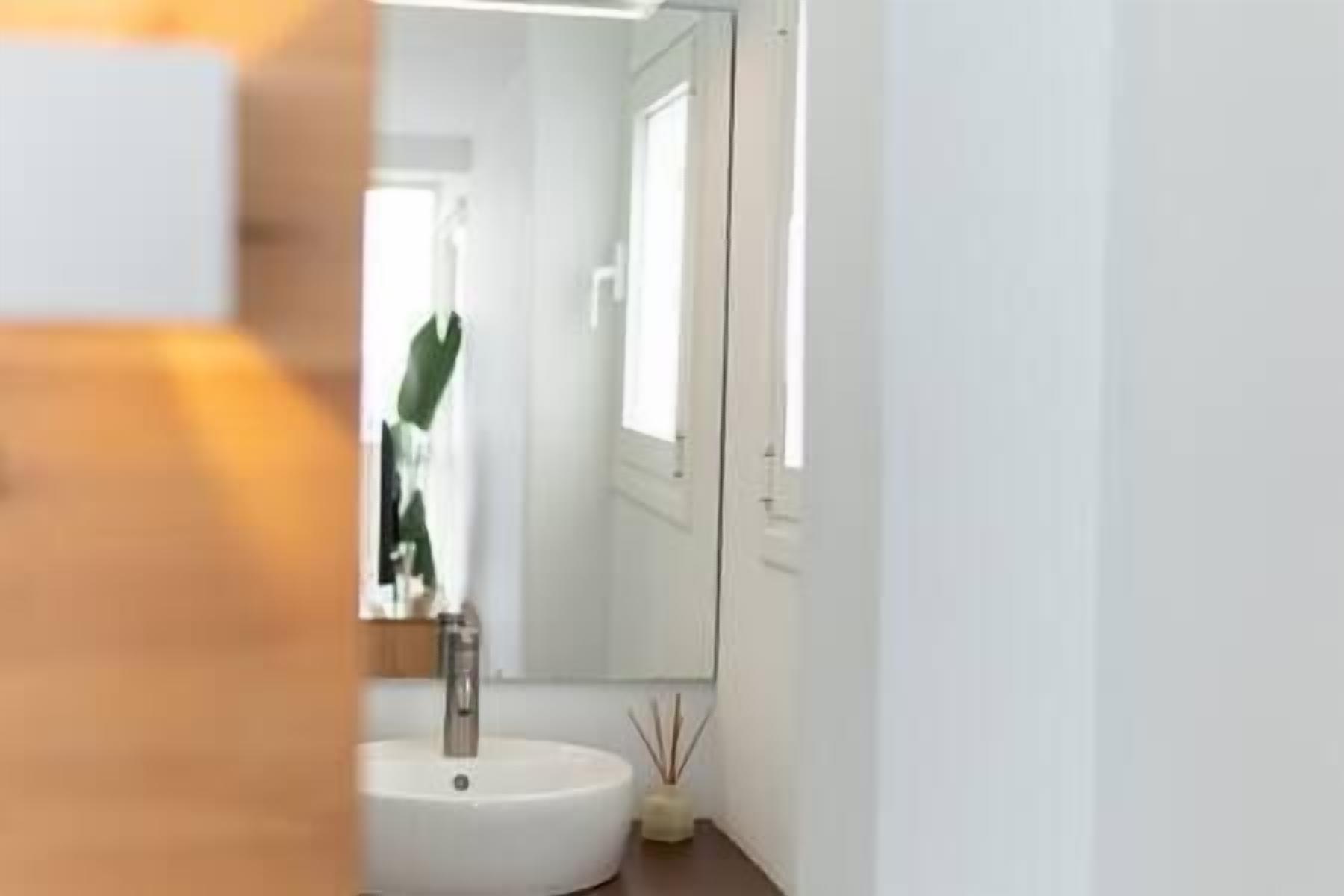 Ein modernes Badezimmer mit einem weißen Waschbecken, einem Spiegel und einer Tür zu einem anderen Raum.
