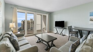 A modern living room with a sofa set, a coffee table, a TV, and a dining area. - Beachfront condo w/ free daily attraction tickets (Panama City Beach)