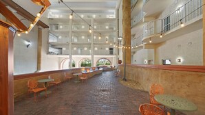 A spacious indoor courtyard with brick flooring, orange chairs, and tables, featuring a high ceiling with multiple balconies and string lights. - Ocean view condo w/ pool and hot tub (Panama City Beach)