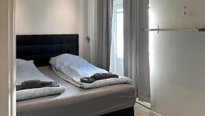A modern bedroom with a black headboard, a bed with grey bedding, a grey rug, and a window with curtains. - Luxury Apartment in City Hotspot (Gothenburg)