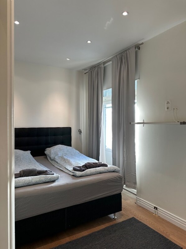 A modern bedroom with a black headboard, a bed with grey bedding, a grey rug, and a window with curtains.