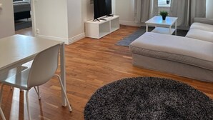 A modern living room with a white sofa, a dining table with chairs, a TV on a white stand, and a large black rug. - Luxury Apartment in City Hotspot (Gothenburg)