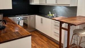 A modern kitchen with white cabinets, a wooden countertop, a stainless steel range hood, and a single bar stool. - Luxury Apartment in City Hotspot (Gothenburg)