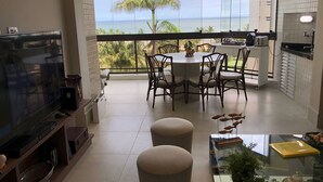 Ein modernes Wohnzimmer mit Fernseher, Sitzecke und einem Balkon mit Meerblick.