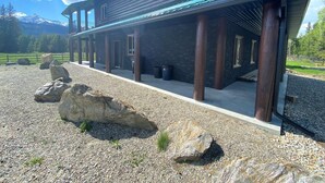 A two-story wooden house with a covered porch, large rocks in the foreground, and a mountain in the background. - Westview Cabin Rental (Valemount)
