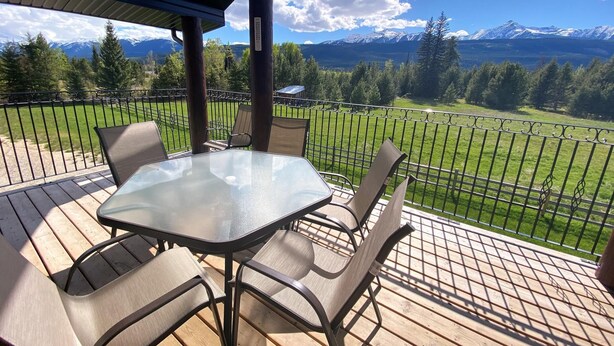 A covered outdoor seating area with a table and chairs, overlooking a mountainous landscape. - Westview Cabin Rental (Valemount)