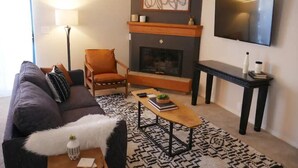 Un salon comprenant un canapé, un fauteuil, une cheminée, un téléviseur et une table basse.