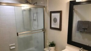 Une salle de bain moderne avec une douche à parois de verre, un lavabo avec un miroir et un tableau encadré au mur.