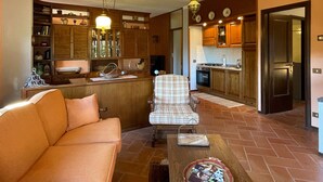 A cozy living room with a sofa, a coffee table, and a dining area with a chair and table. The kitchen has wooden cabinets and a stove.