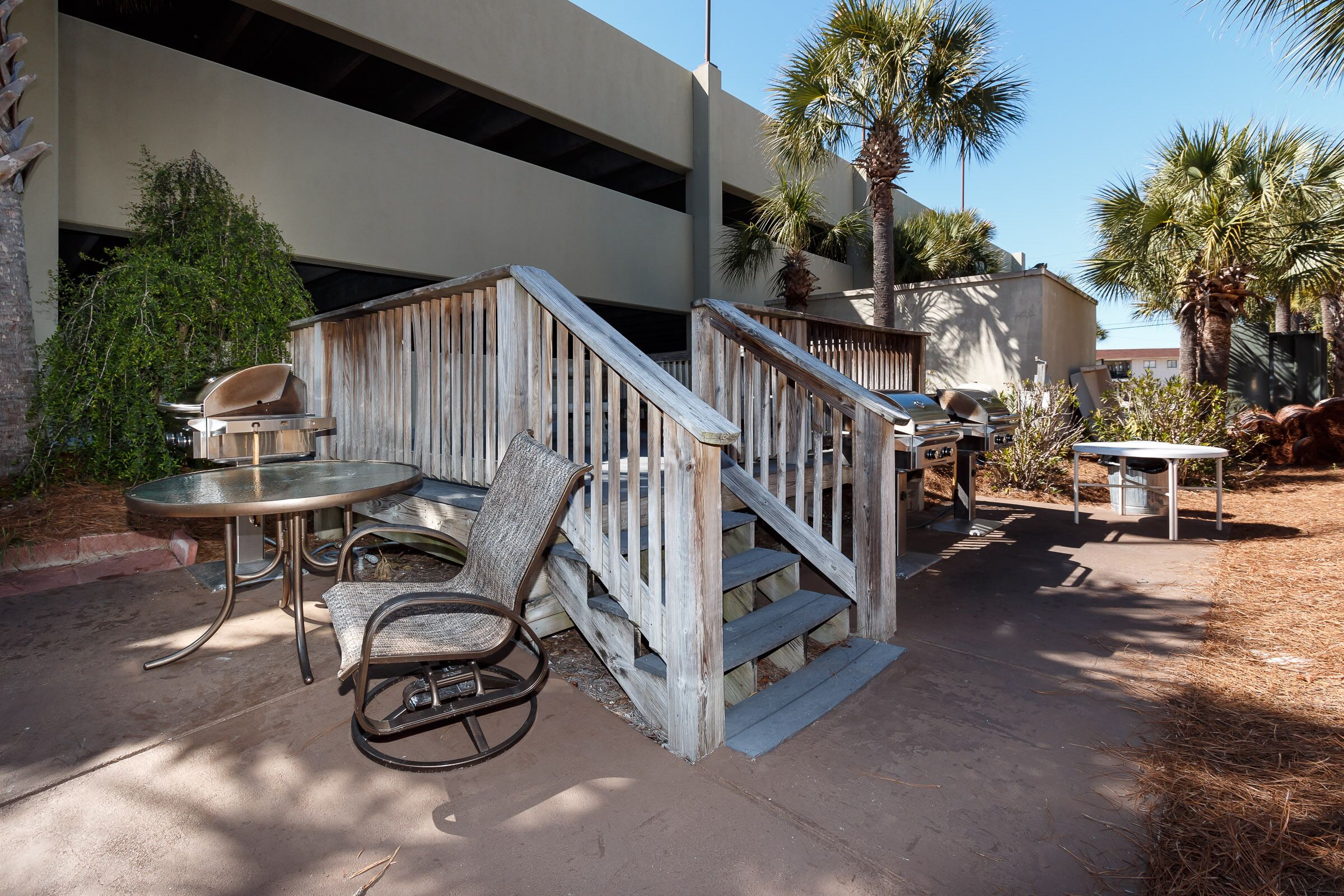 A patio area with a wooden staircase, outdoor seating, and a grill.