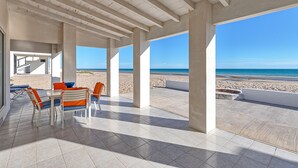 An open terrace with a view of the beach, featuring a table with chairs and a view of the ocean.