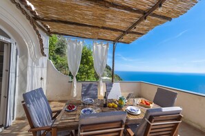 An outdoor dining area with a table set for two, overlooking a scenic view of the sea.