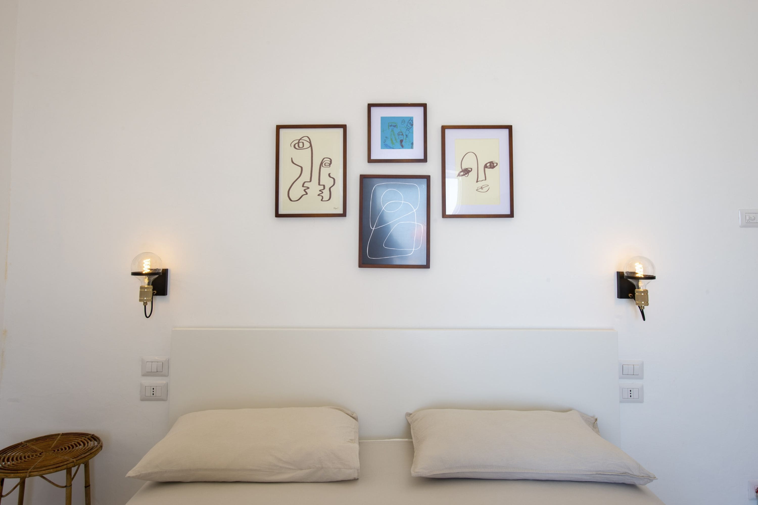 A bedroom with a bed, two wall-mounted light fixtures, and three framed artworks on the wall.