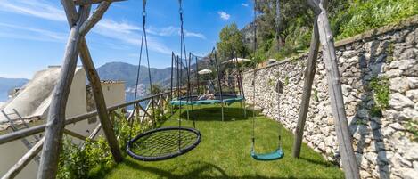 A wooden swing set with a netted swing, a trampoline, and a stone wall.