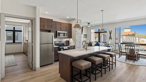 A modern kitchen with a central island, stainless steel appliances, and a large window offering a view of the city. - Skywalk Flats Mountainview Condo: Downtown, Rooftop Hot Tubs (Silverthorne)