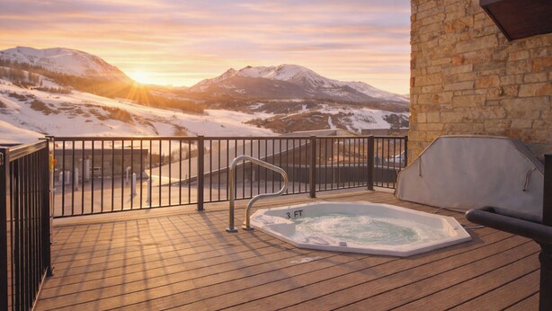 A wooden deck with a hot tub, a stone wall, and a mountain view. - Skywalk Flats Mountainview Condo: Downtown, Rooftop Hot Tubs (Silverthorne)