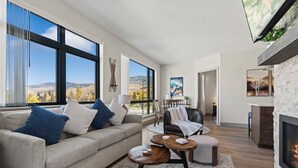 A modern living room with a large window, a fireplace, and a view of the mountains. - Skywalk Flats Mountainview Condo: Downtown, Rooftop Hot Tubs (Silverthorne)