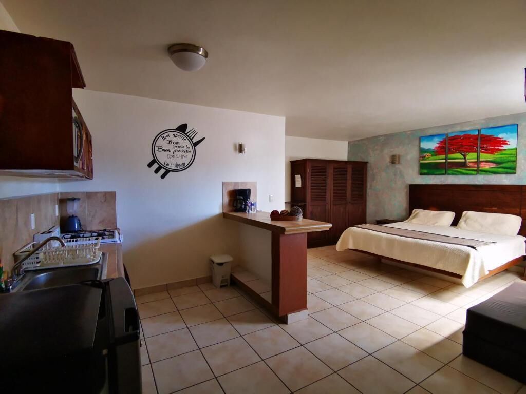 Una habitación de hotel compacta con kitchenette, una cama, un cuadro de un árbol y un baño pequeño.
