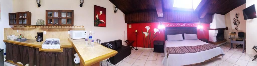 Une chambre d’hôtel équipée d’une kitchenette, d’un lit, d’un mur d’accent rouge et d’un téléviseur.