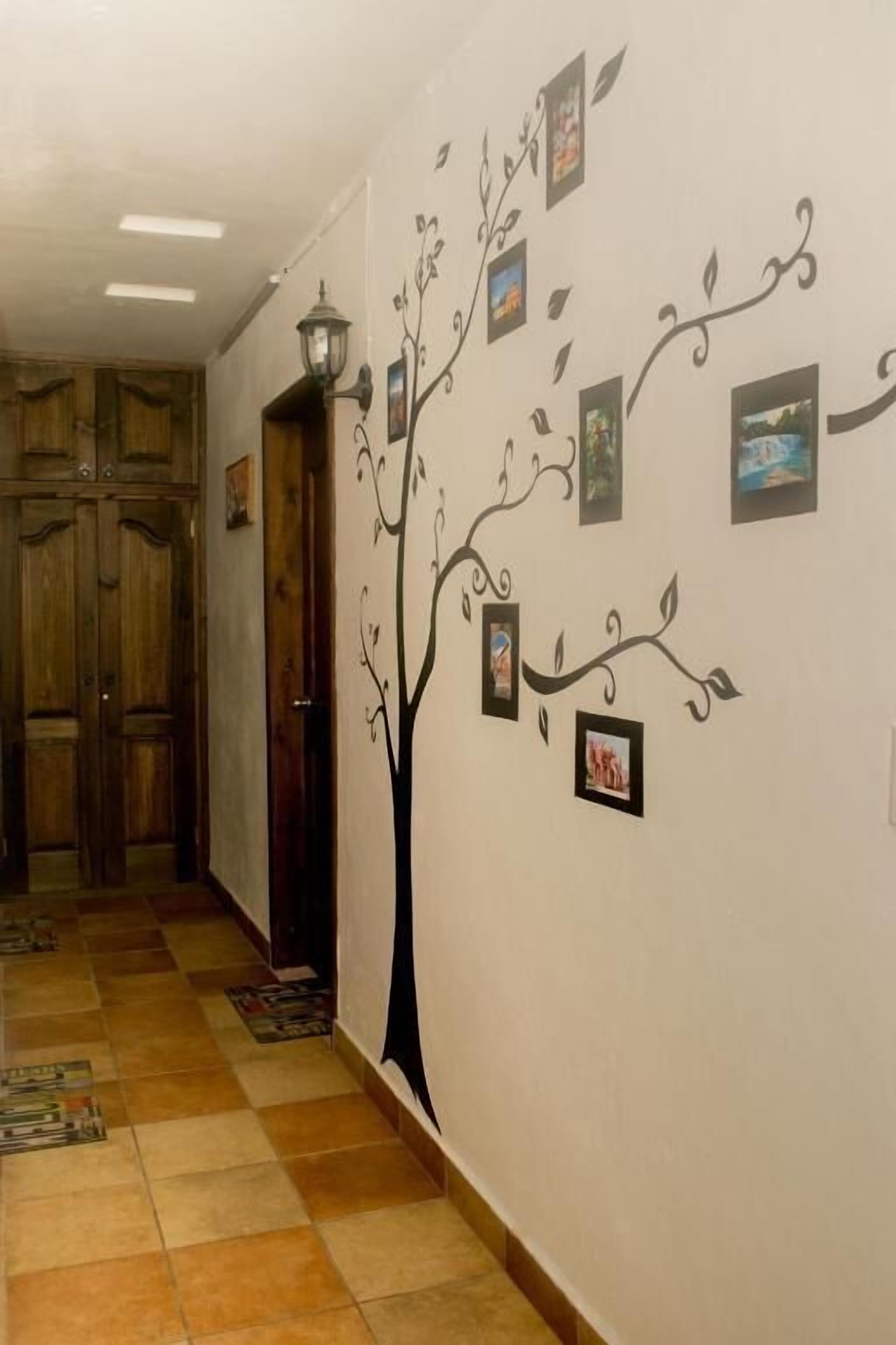 A hallway with a wall mural of a tree with photos, wooden doors, and a tiled floor.