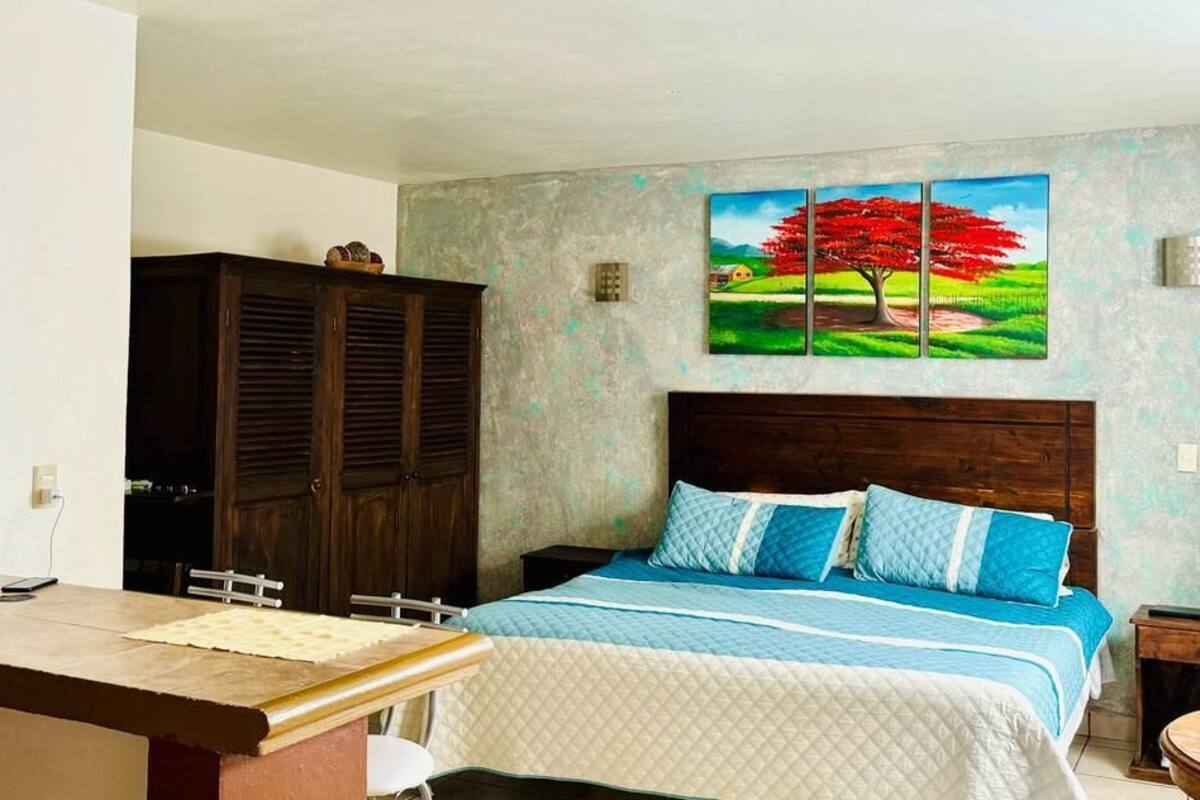 Un dormitorio con una cama, un armario de madera, un escritorio y un cuadro de un árbol en la pared.