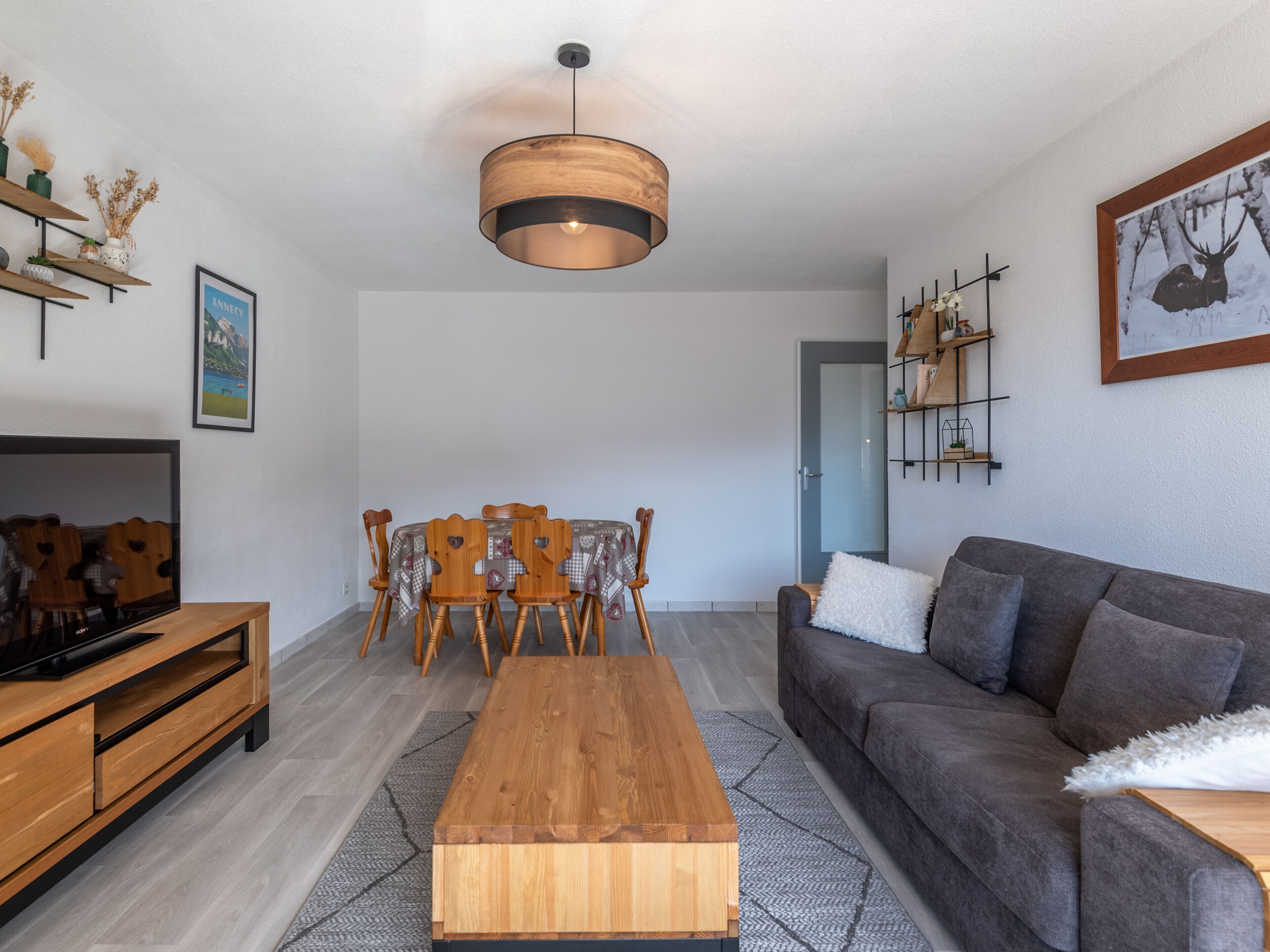 A modern living room with a wooden coffee table, grey sofa, and a dining area with a wooden table and chairs.