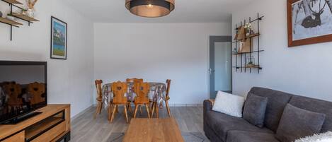 A modern living room with a wooden coffee table, grey sofa, and a dining area with a wooden table and chairs.