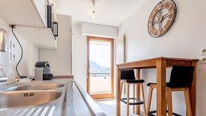 A modern kitchen with stainless steel appliances, a wooden table with two chairs, and a large wall clock.
