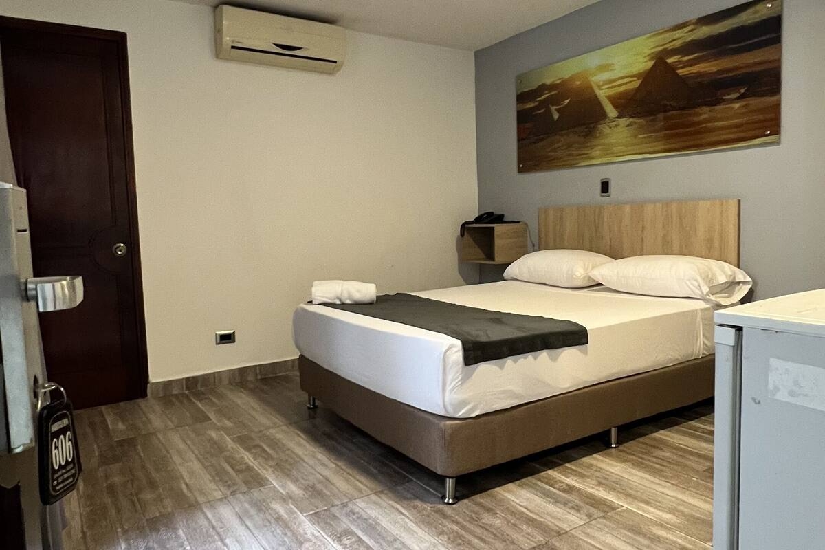Een hotelkamer met een bed, een schilderij aan de muur, een deur en een kleine koelkast.