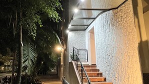 Ein Gebäude nachts, mit einer Treppe, die zu einer Tür führt, umgeben von Bäumen und einem gefliesten Weg.