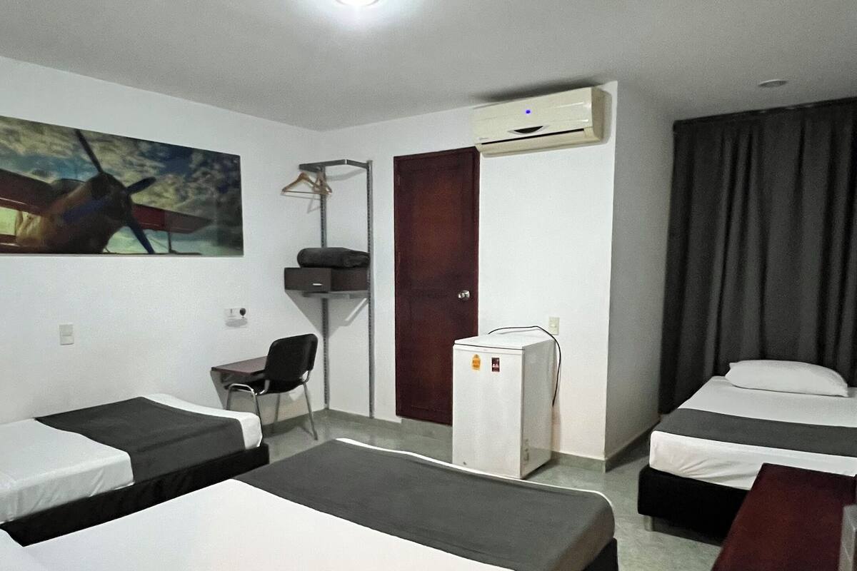 Een hotelkamer met twee eenpersoonsbedden, een bureau, een stoel, een kleine koelkast en een airconditioning.