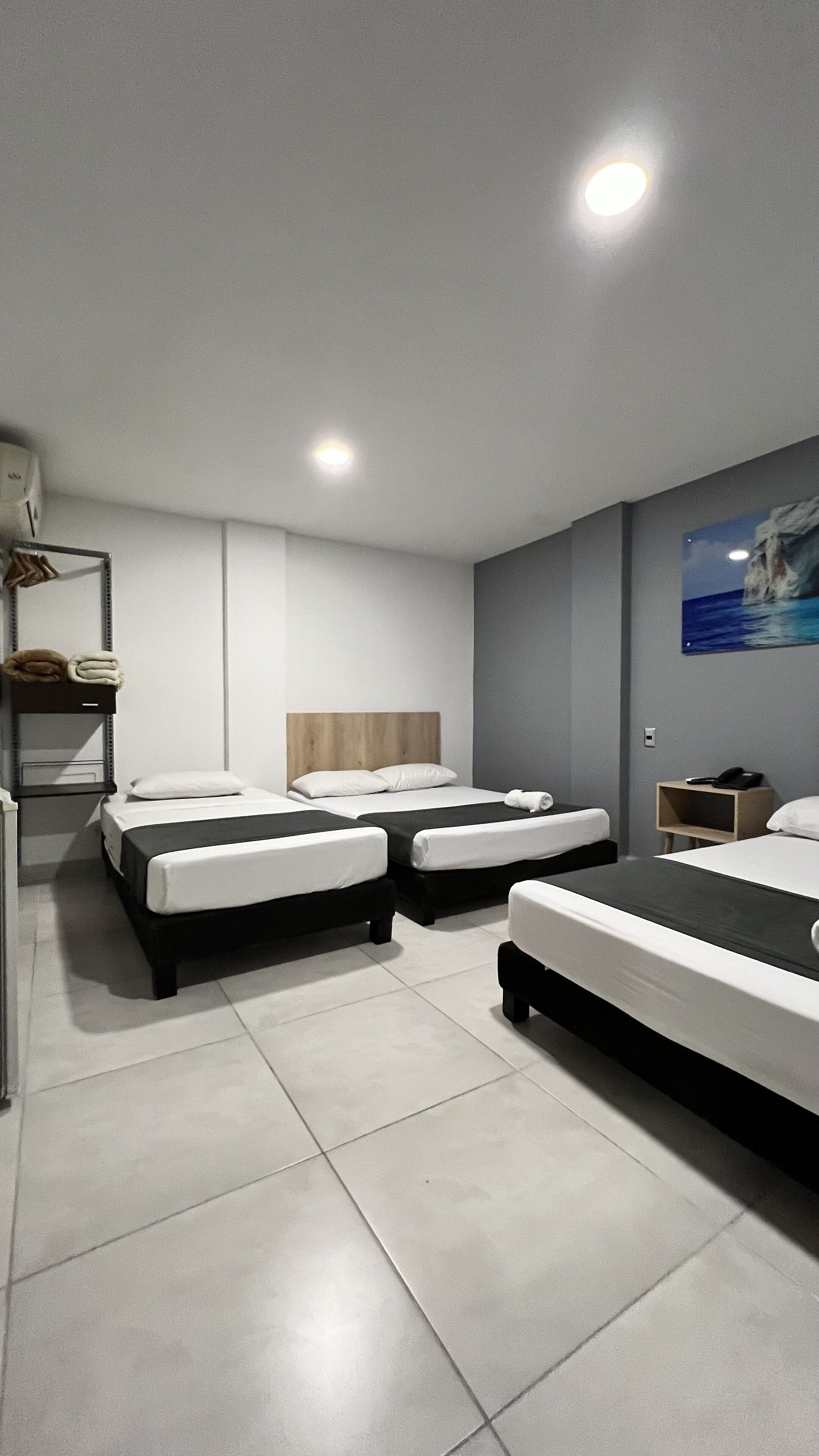 Een moderne hotelkamer met twee bedden, een houten hoofdbord, een schilderij aan de muur en een klein nachtkastje met een telefoon.