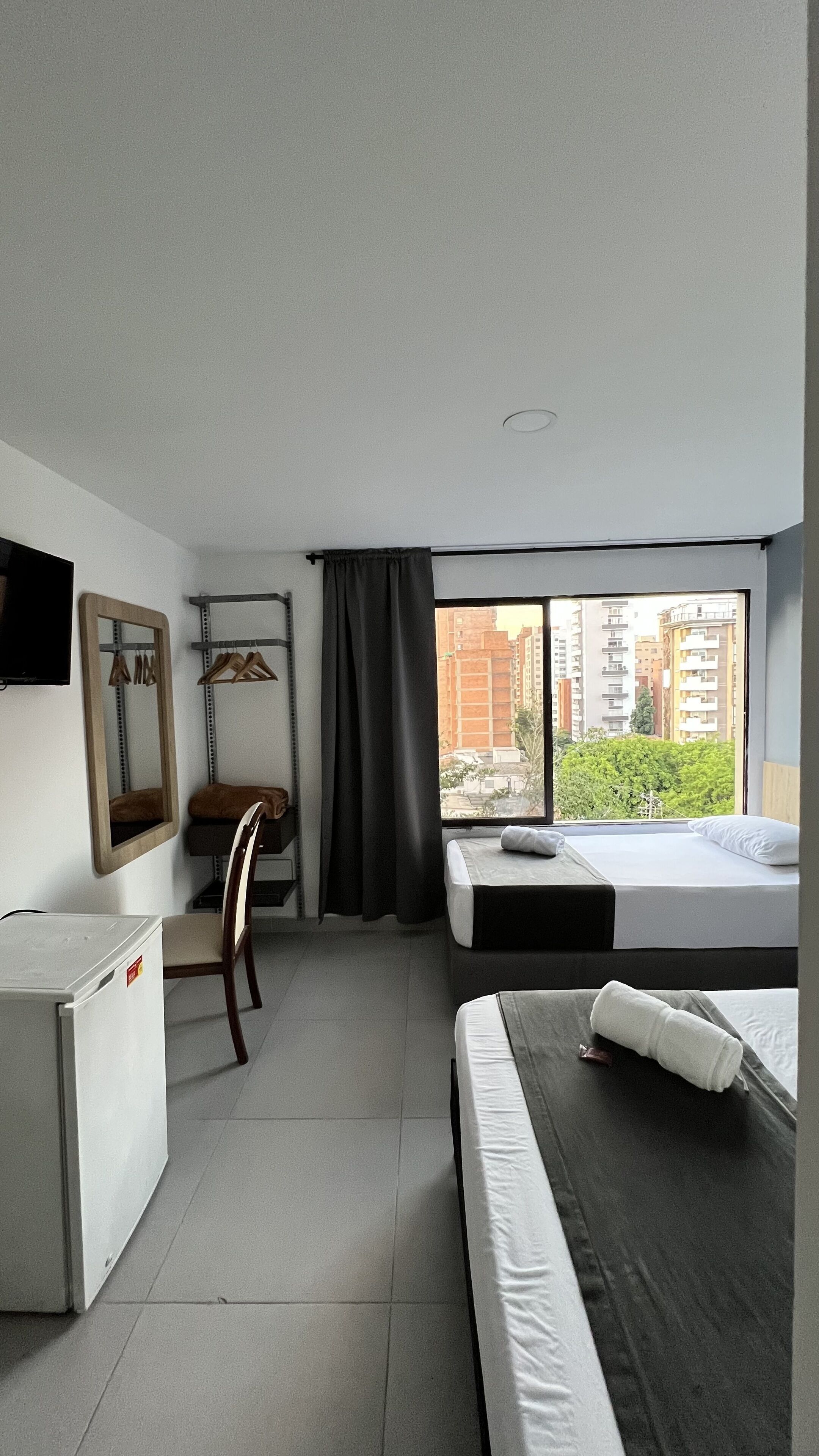 Une chambre d’hôtel équipée d’un lit, d’un bureau, d’une chaise, d’un miroir et d’une fenêtre donnant sur la ville.