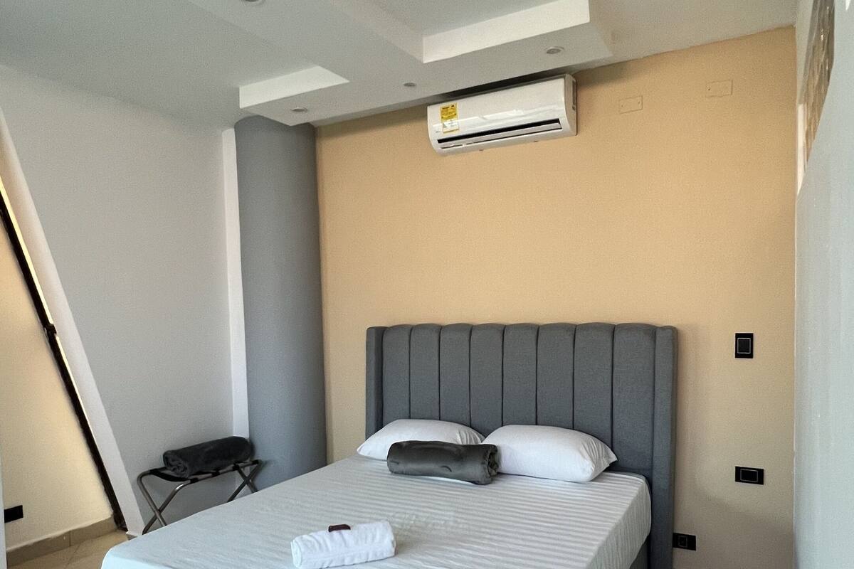Een moderne slaapkamer met een groot bed, een grijs hoofdeinde en een aan het plafond gemonteerde airconditioner.